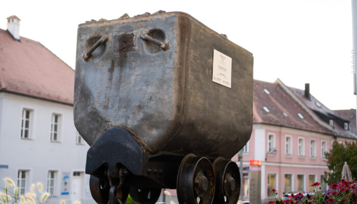 Bergbaulore vor dem alten Amtsgericht, dem heutigem Literaturarchiv in Sulzbach-Rosenberg. Eine Lore ist ein kleiner Förderwagen, der im Bergbau verwendet wurde. Eine von vielen Stationen entlang des Bergbaupfades.