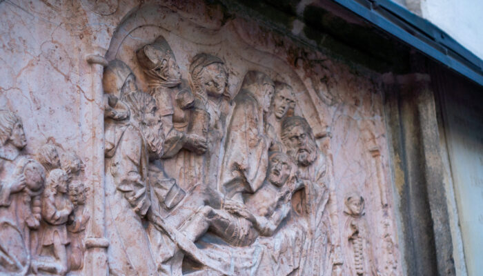 Epitaphien der Kirche St. Marien von links aufgenommen. Epitaphien sind Gedächtnissteine von Verstorbenen, die an sie erinnern sollen. Diese sind künstlerisch meist aufwendig gestaltet und befinden sich gerade im Landkreis Amberg-Sulzbach oftmals an Kirchen, wie hier in St. Marien in Sulzbach-Rosenberg. Die meisten Epitaphien sind von Hammerherren ab dem Mittelalter gestiftet worden und sollten zum einen an den Verstorbenen erinnern, aber auch ein klein wenig an seine Frömmigkeit. Diese Frömmigkeit zeigt sich in der künstlerischen Umsetzung mit Szenen aus der Bibel, die der Stifter oder die Hinterbliebenen in Auftrag gaben. Die Kirche St. Marien hat einige Epitaphien, u.a. die der Hammerherrenfamilie Frank. Der Künstler hat hier die Szene dargestellt, wie Jesus ins Grab gelegt wird. Interessant sind aber die Figuren rechts und links neben dem großen Hauptbild. Rechts die Nonne mit Rosenkranz im Gebet und links die Gruppe mit einem Mönch, ebenfalls mit Rosenkranz im Gebet. Da im Mittelalter die Vergebung der Sünden immens wichtig war, dürfte dieser Gedächtnisstein das Ziel der Familie gewesen sein. Ihre Frömmigkeit im Gebet mit dem Rosenkranz zeigen und die damit verbundene Vergebung der Sünden des Verstorbenen und der Familie.