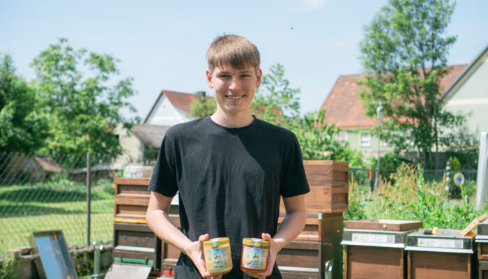 Jungimker Jannik, wie er den fertigen Honig in zwei Honiggläsern präsentiert